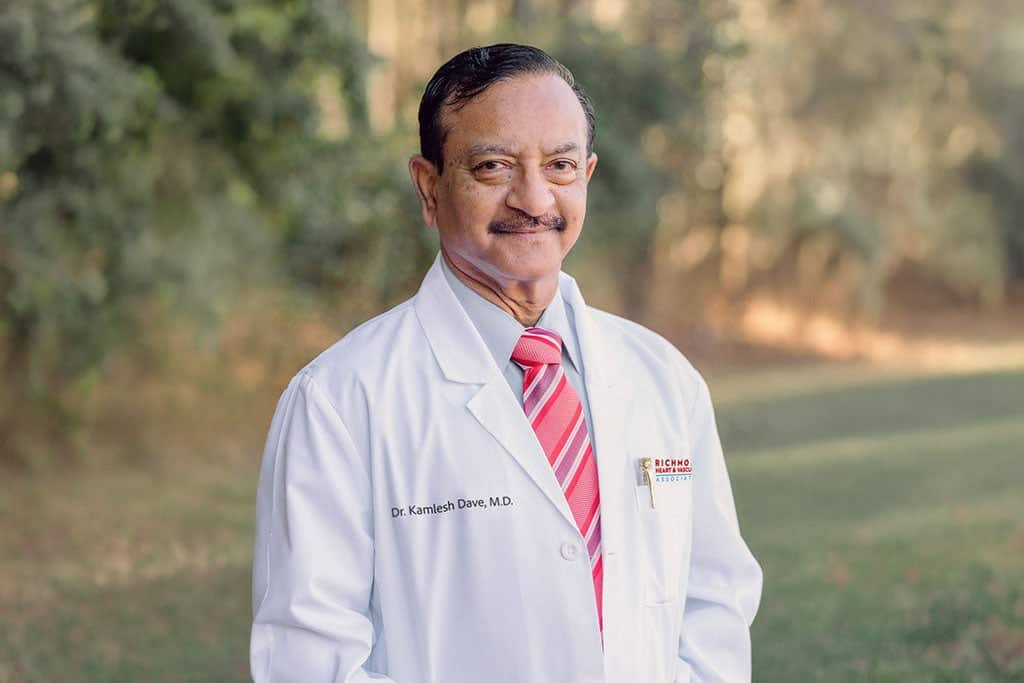 Interventional cardiologist smiling in a white lab coat outdoors for a professional provider portrait of Kamlesh Dave, MD