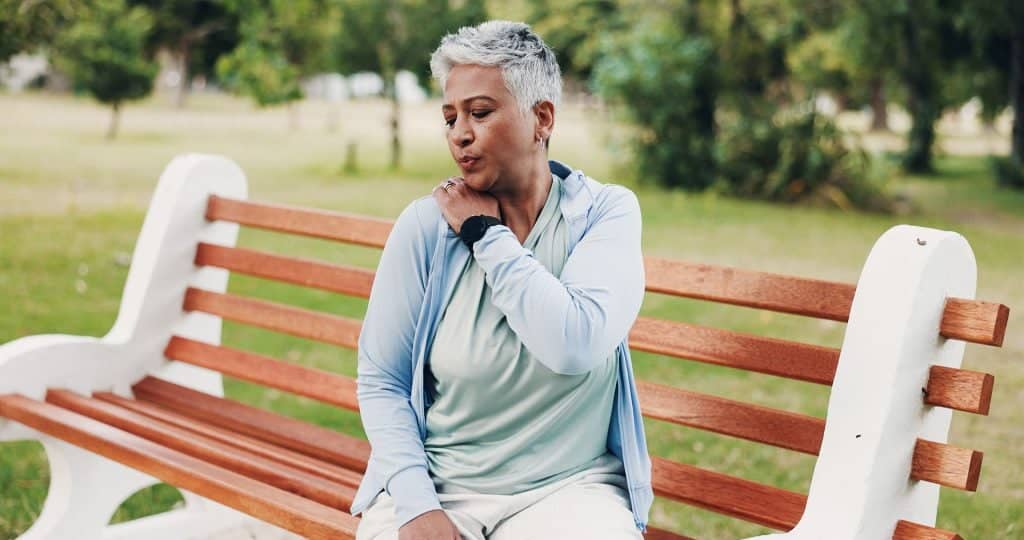 Senior woman holding her shoulder while resting on a park bench during outdoor exercise for Peripheral Arterial Disease Treatment