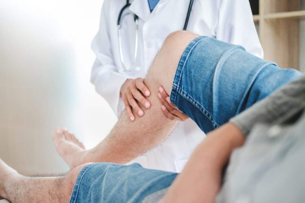 Doctor examining and palpating a patient's elevated leg on an examination table during a clinical evaluation for Deep Vein Thrombosis and Venous Insufficiency